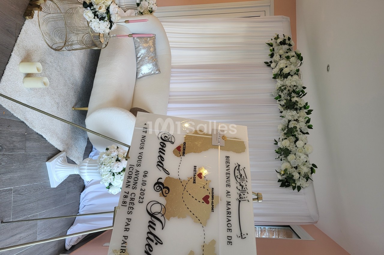 Panneau de bienvenue à un mariage devant un décor floral blanc avec canapé et bougies dans une salle lumineuse.