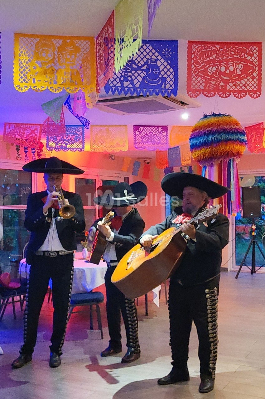 Musiciens mariachi jouant de la trompette, de la guitare et du violon dans une salle décorée de couleurs vives et de…