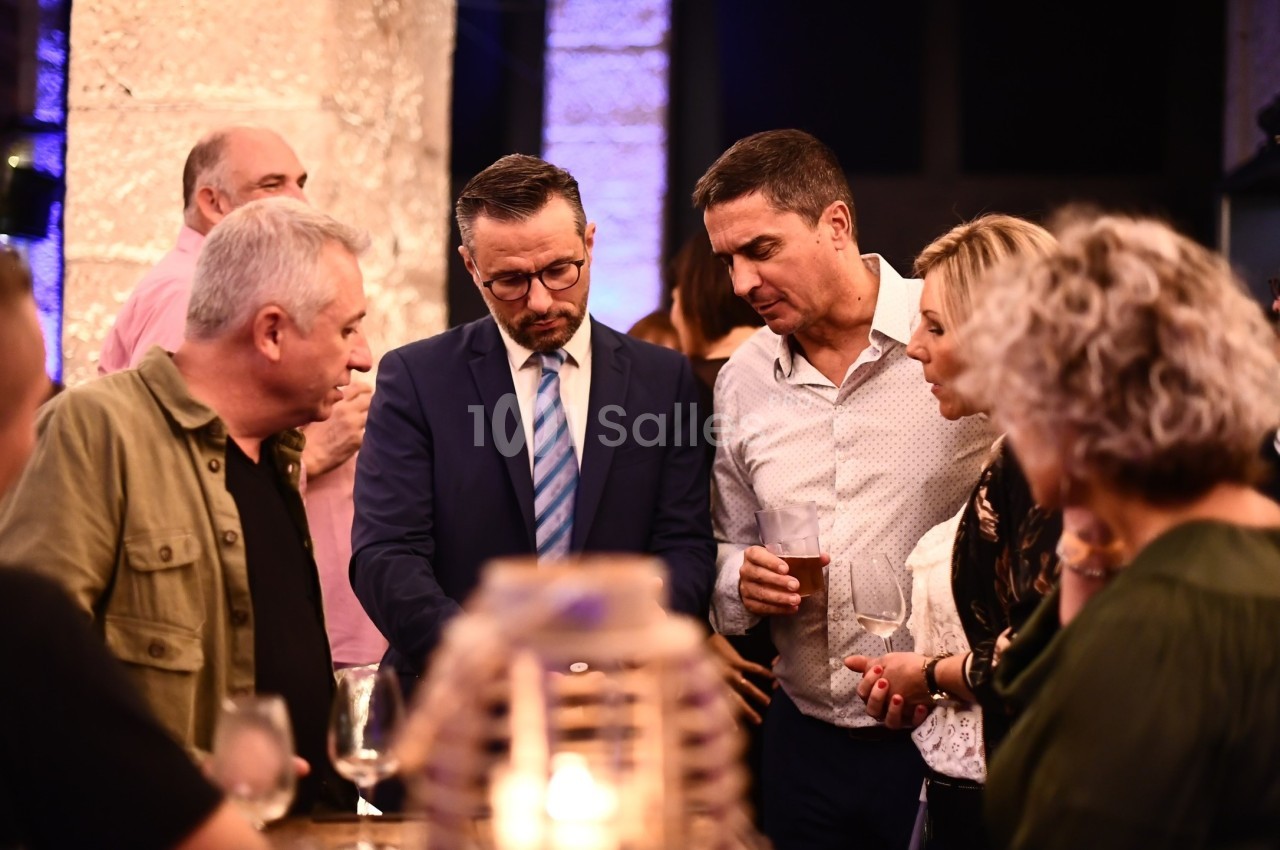 Un groupe de personnes discute autour d'une table lors d'un événement en intérieur, éclairé par une lumière chaleureuse.