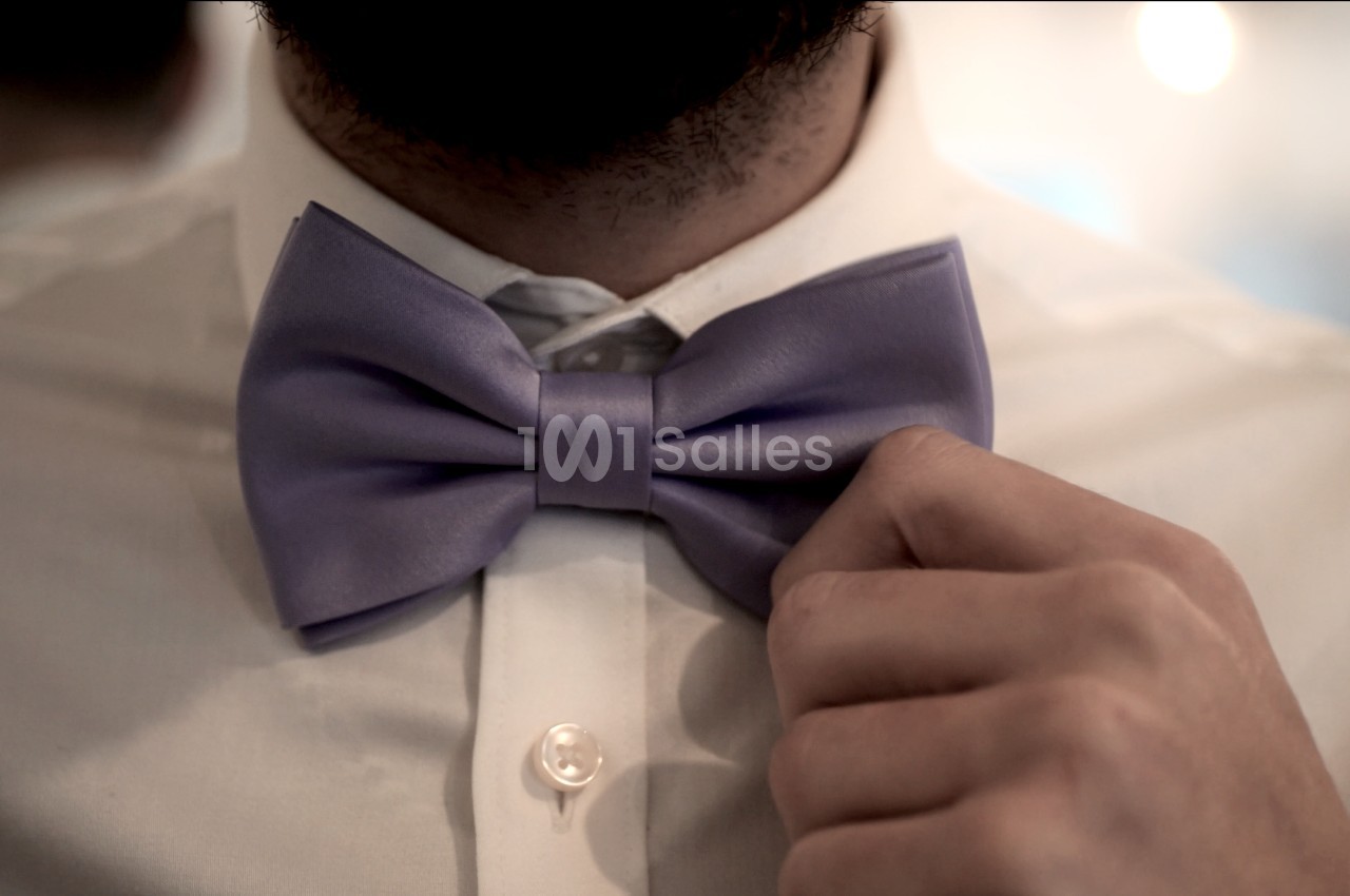 Un homme ajuste un nœud papillon violet sur une chemise blanche.