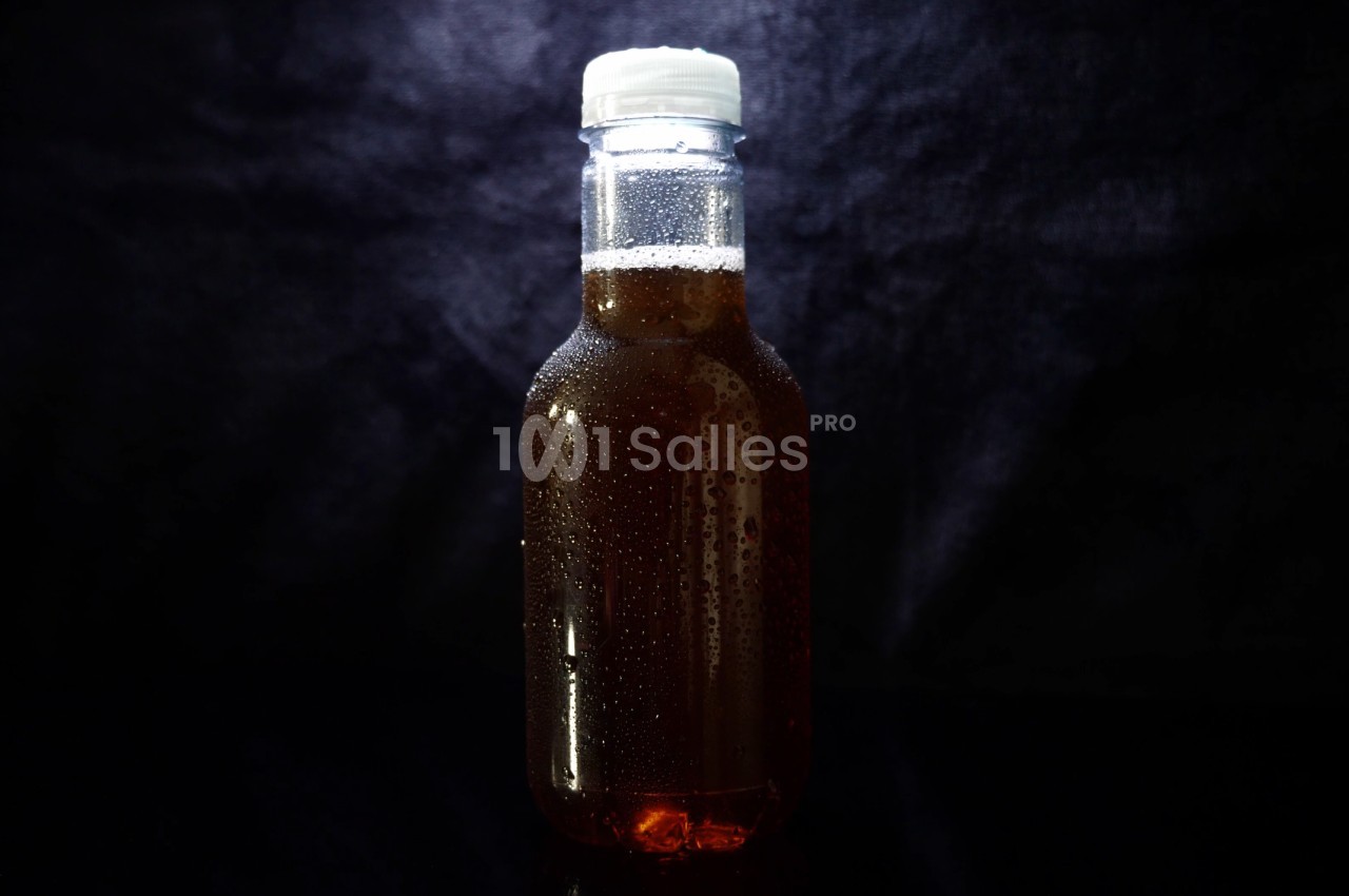 Bouteille en verre remplie de liquide brun, fermée par un bouchon blanc, sur un fond sombre.