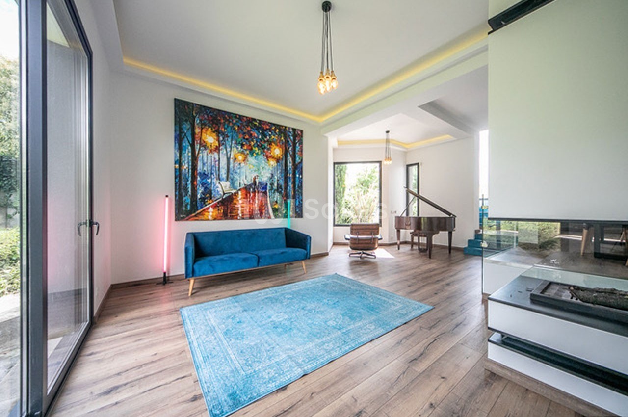 Salon lumineux avec un canapé bleu, un tapis turquoise, un piano et une grande peinture colorée sur le mur.