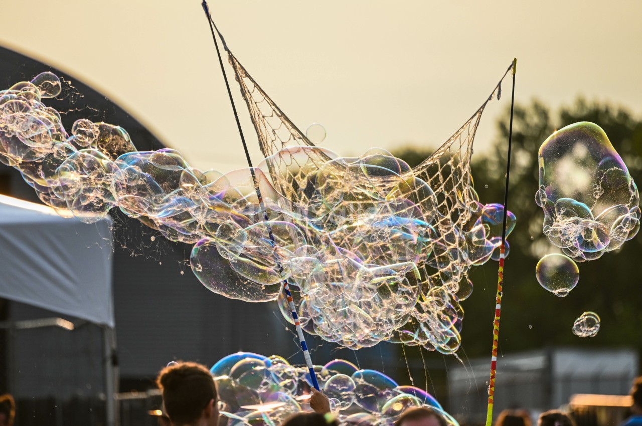 Bulles de savon colorées flottant dans l'air, créées avec un filet lors d'un événement en extérieur.