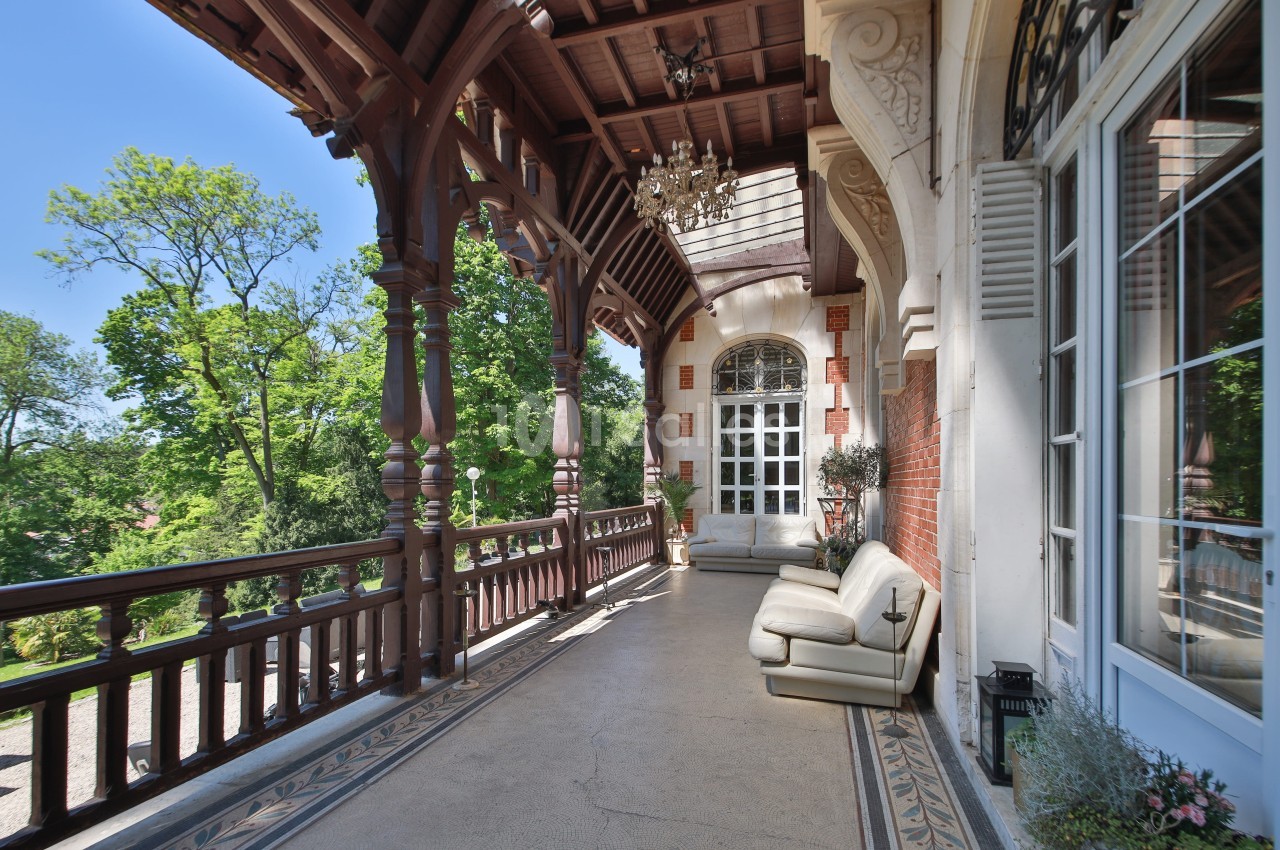 Terrasse couverte avec balustrade en bois, canapé blanc, plantes en pot et vue sur un jardin verdoyant.