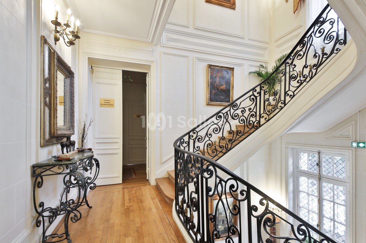 Escalier en colimaçon avec rampe en fer forgé, dans un intérieur lumineux avec parquet et décorations murales.