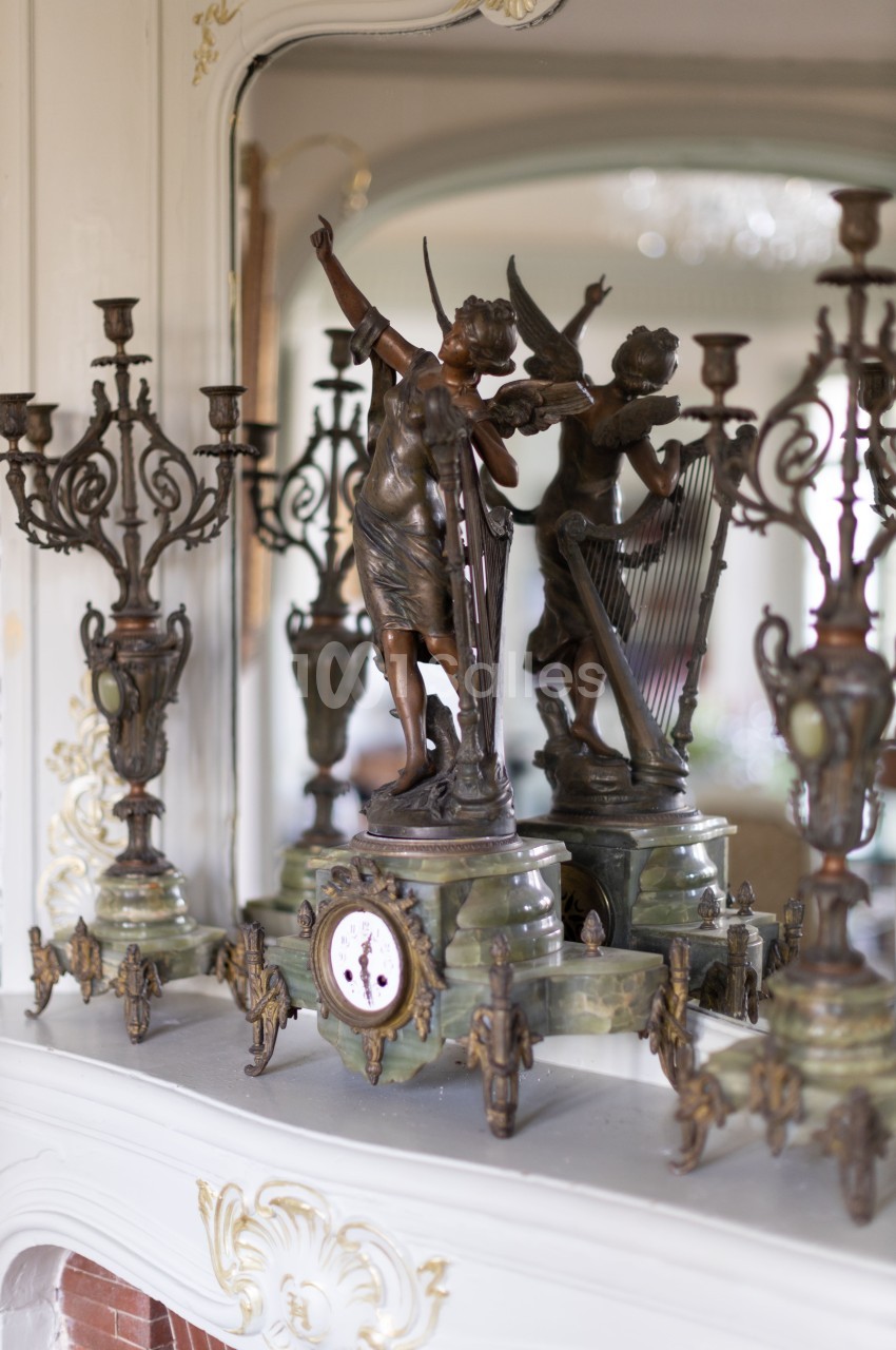 Statue en bronze représentant deux figures féminines avec des candélabres et une horloge sur une cheminée ornée.