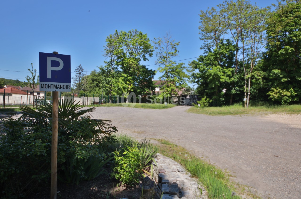 Panneau indiquant un parking nommé ’Montmanoir’ près d'une zone dégagée entourée de végétation et d'arbres.