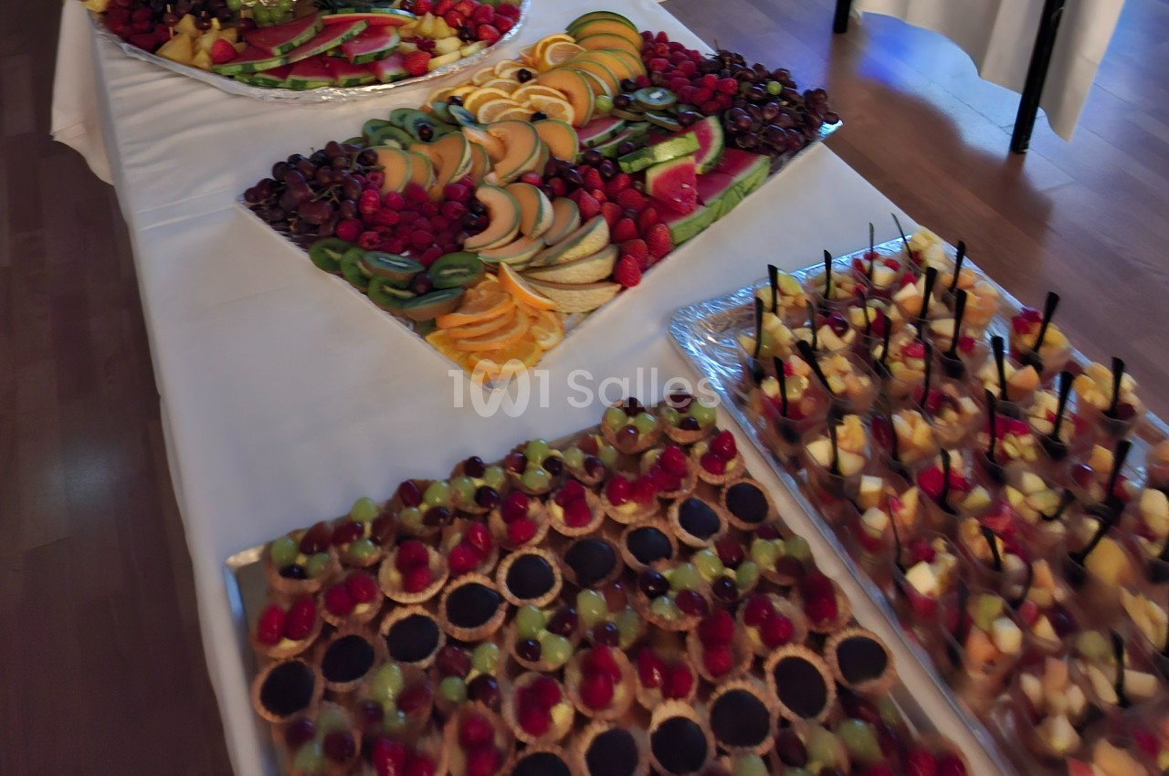Plateau de desserts variés avec tartelettes aux fruits, verrines et assortiments de fruits frais sur une table blanche.
