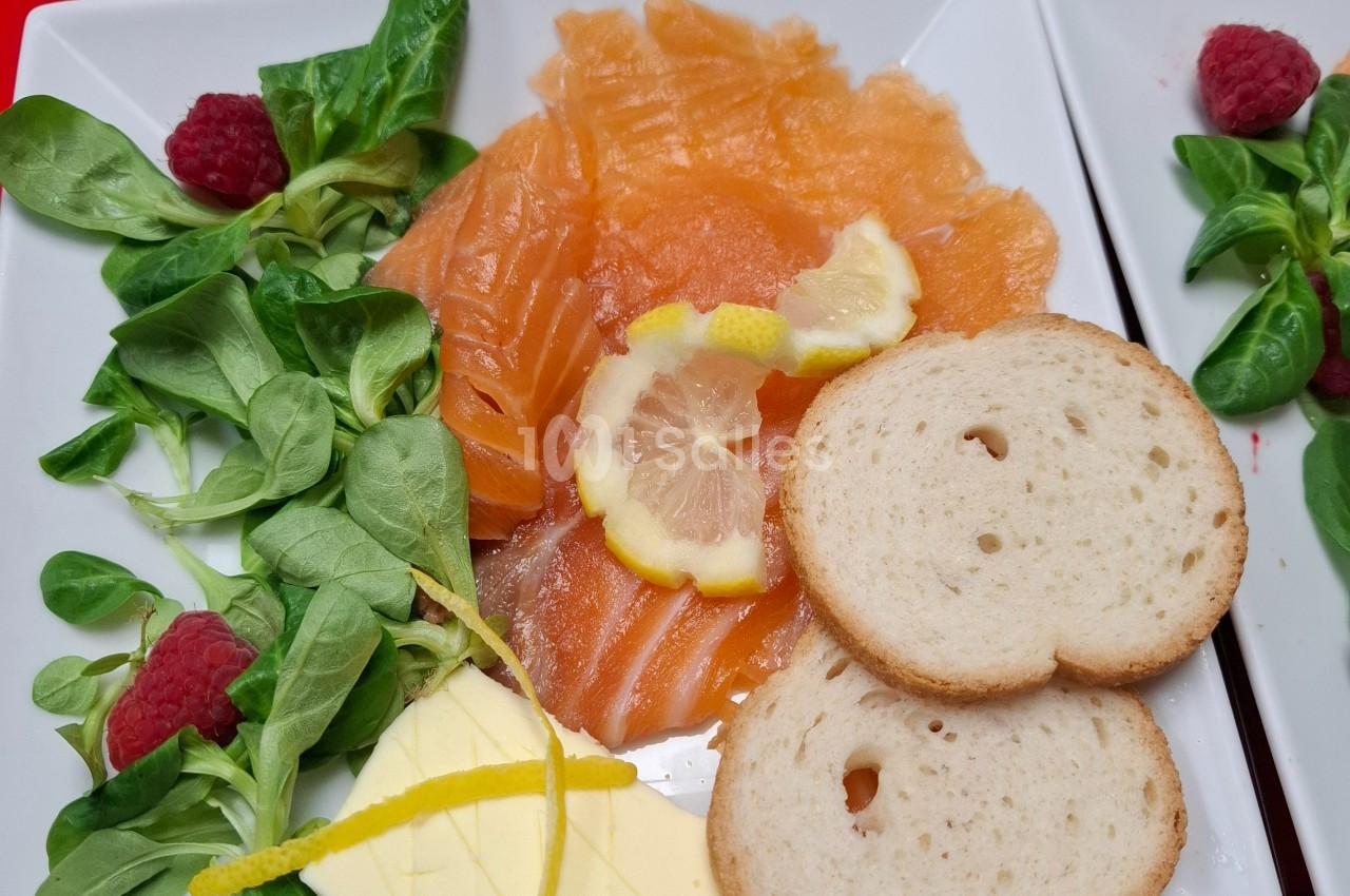 Assiette avec saumon fumé, tranches de citron, mâche, framboises, beurre et rondelles de pain.
