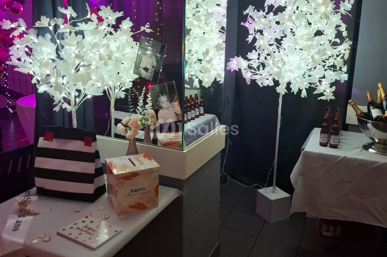 Décoration festive avec arbres lumineux blancs, photo encadrée, boissons et cadeaux sur une table.