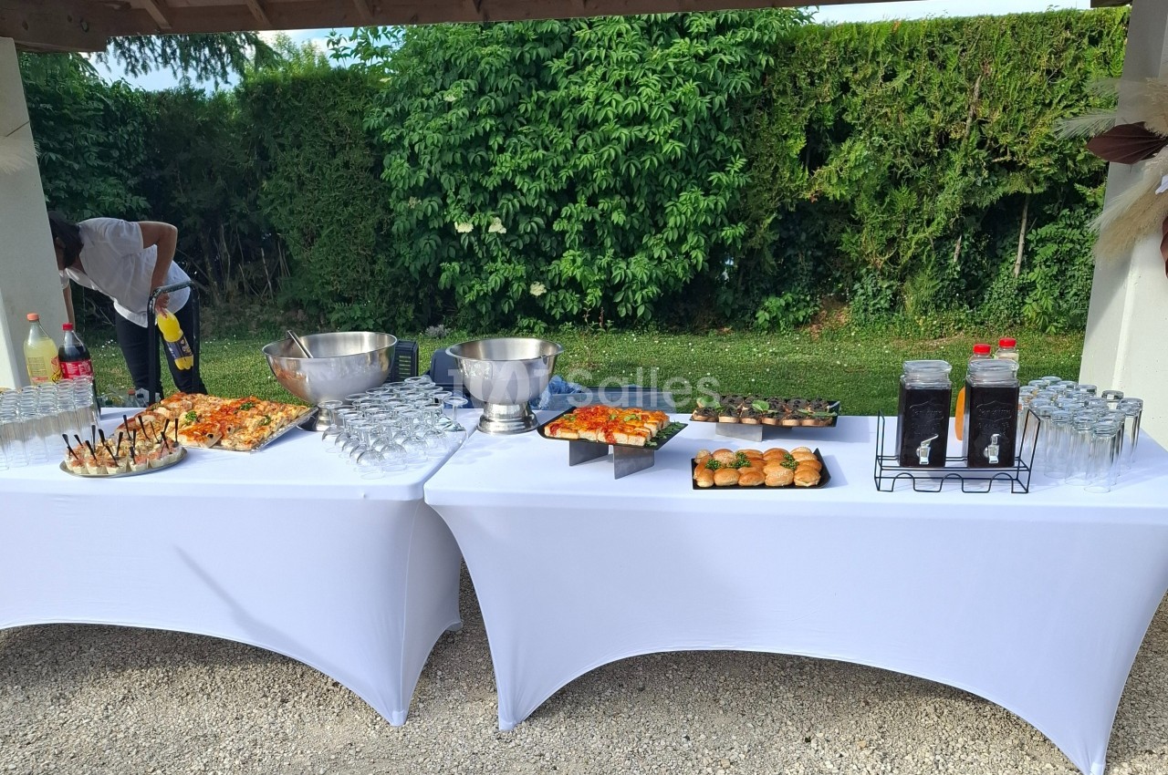 Buffet en extérieur avec tables blanches, proposant boissons, verrines, pizzas, mini-burgers et desserts.