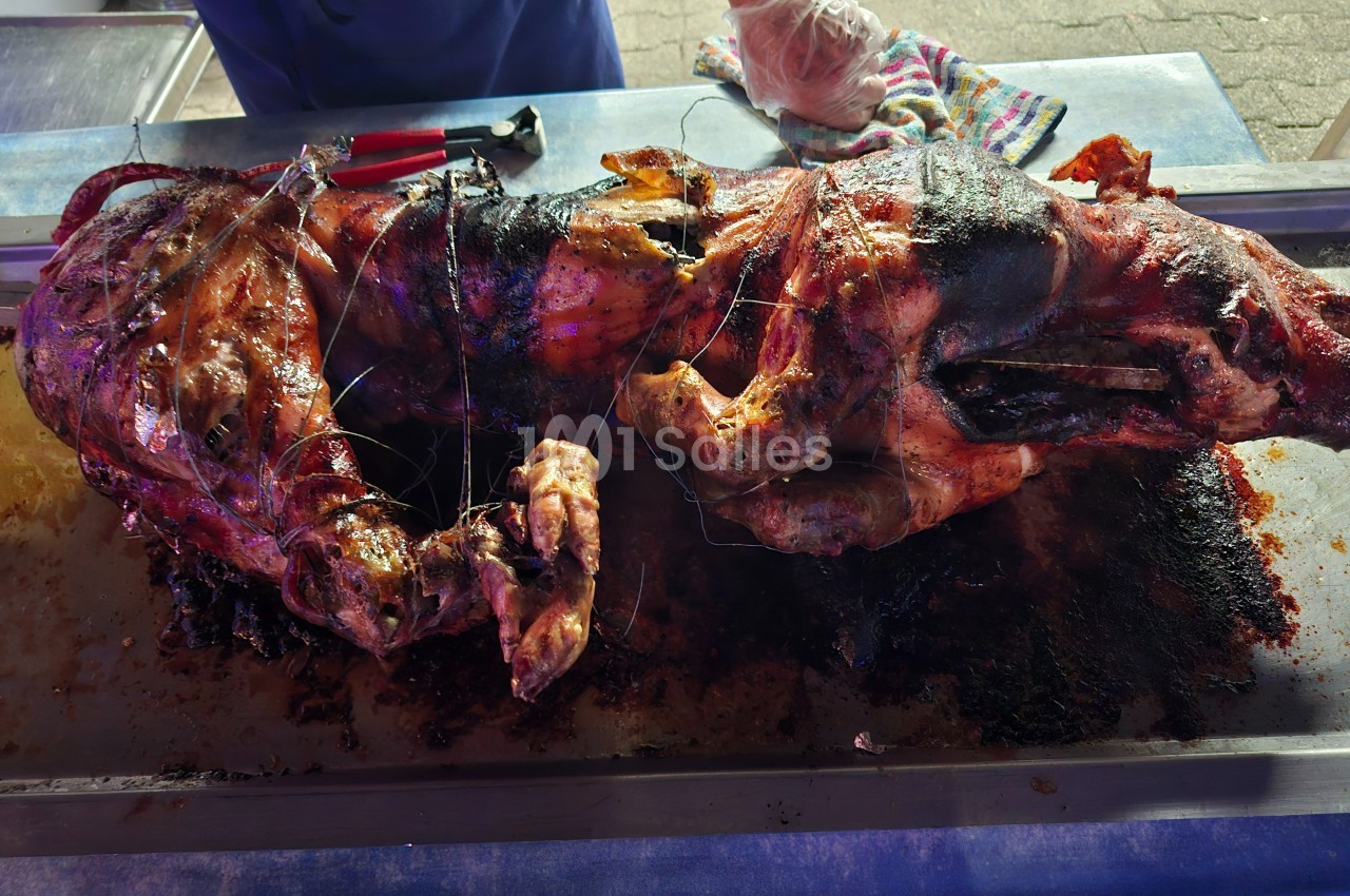 Cochon entier rôti sur une broche, posé sur un plateau métallique, avec des ustensiles en arrière-plan.