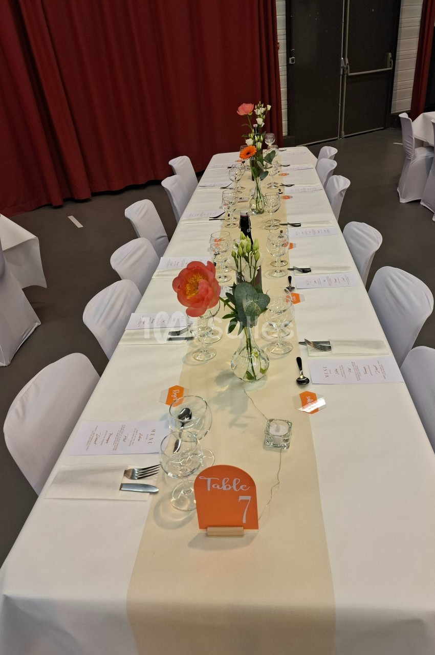 Table dressée avec une nappe blanche, des fleurs colorées en centre de table et des menus disposés pour un repas.