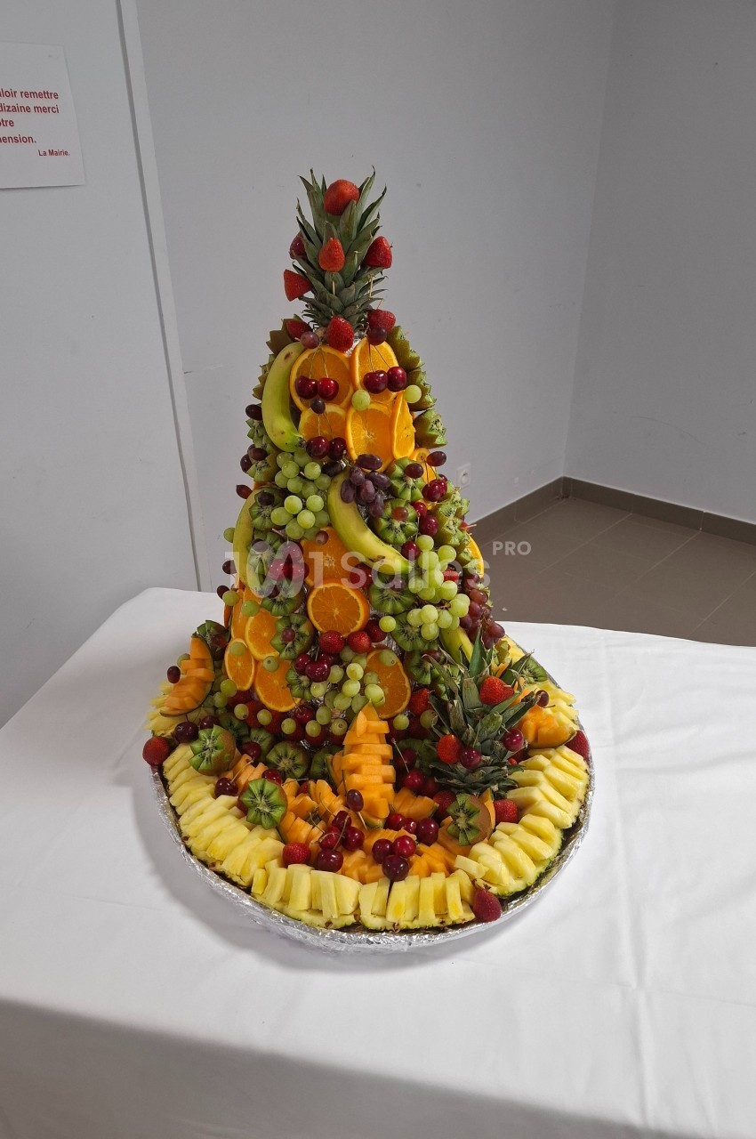 Pyramide de fruits frais variés, incluant ananas, raisins, fraises et oranges, présentée sur un plateau rond.