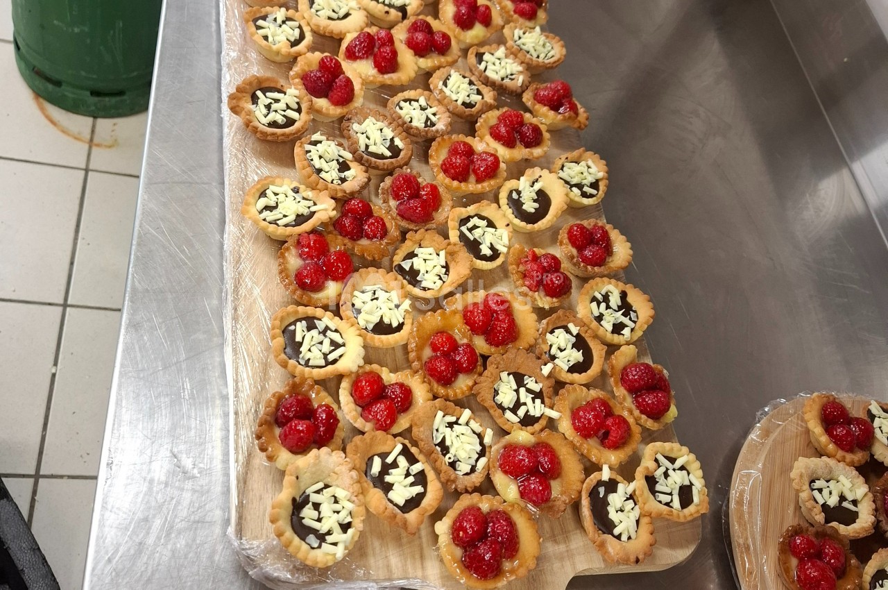Plateau de tartelettes garnies de chocolat, éclats de chocolat blanc et framboises, disposé sur un plan de travail en…
