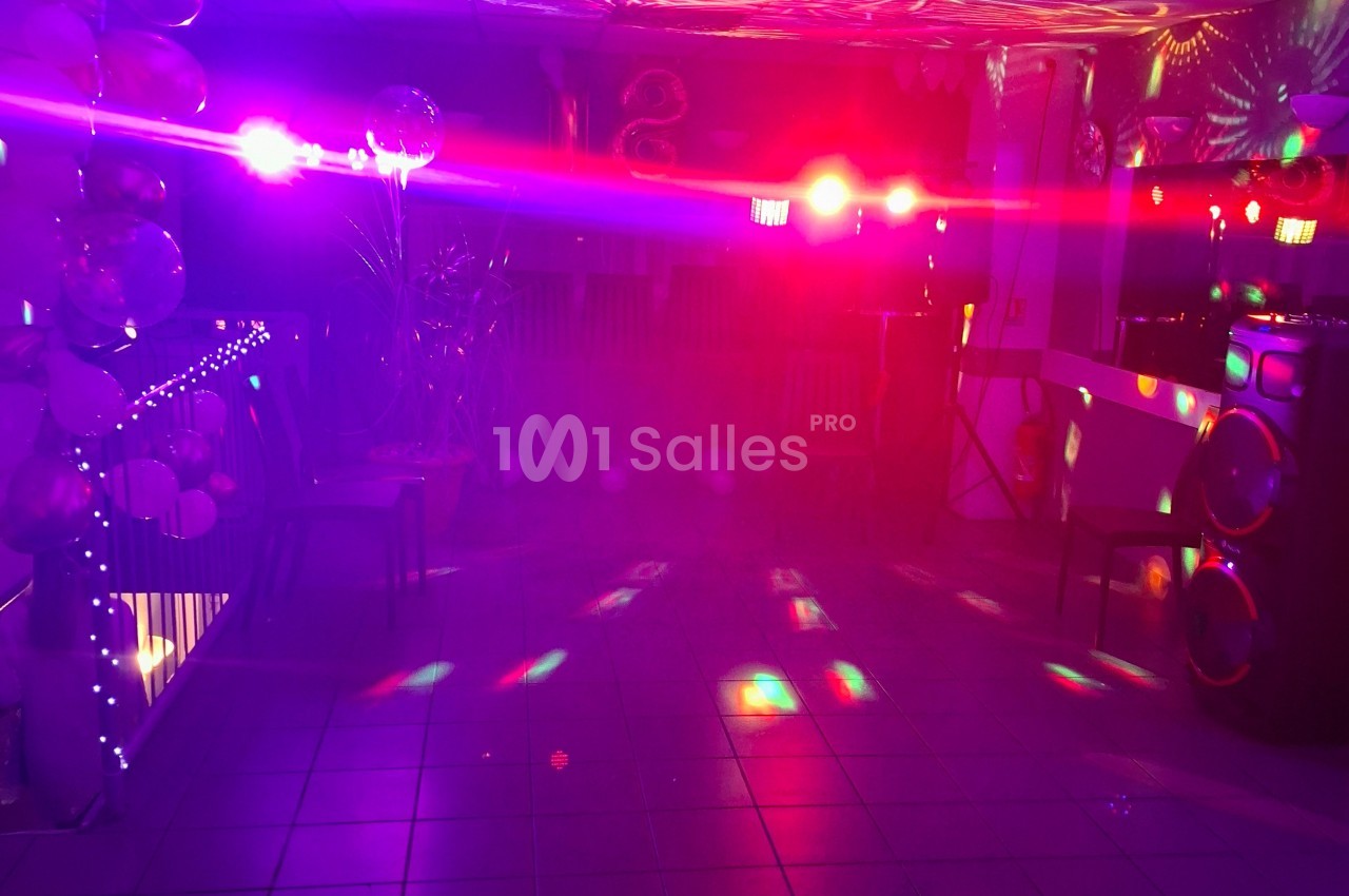 Salle éclairée par des lumières colorées avec des spots et des reflets sur le sol carrelé.