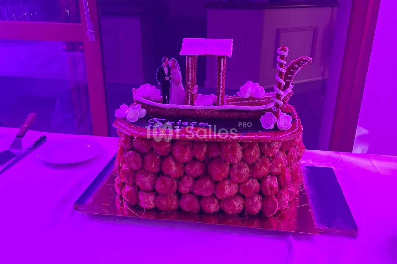 Pièce montée en choux décorée d'une gondole en sucre avec des figurines de mariés, éclairée par une lumière violette.