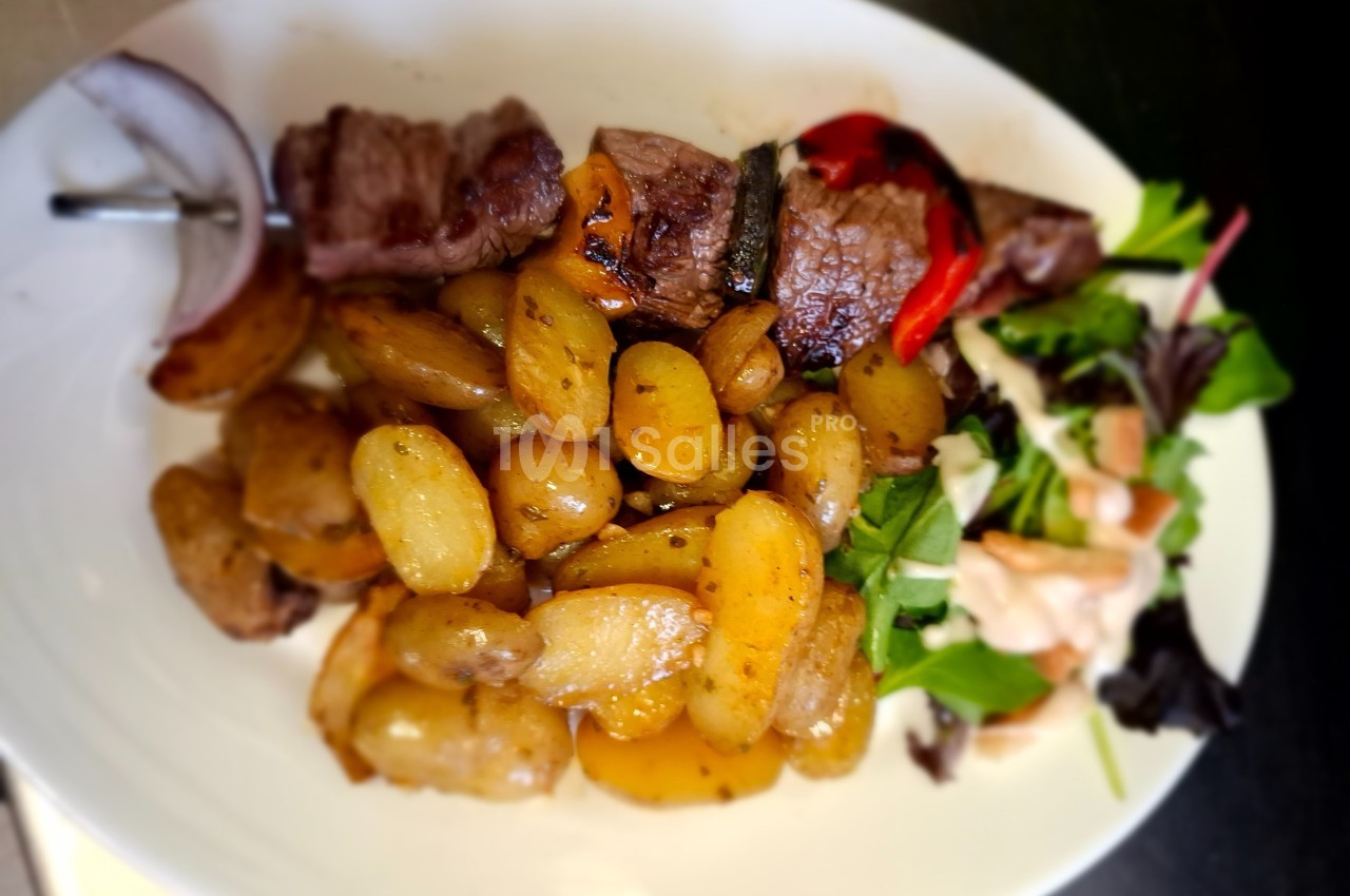 Assiette contenant des pommes de terre rôties, brochette de viande, légumes grillés et salade verte avec sauce.