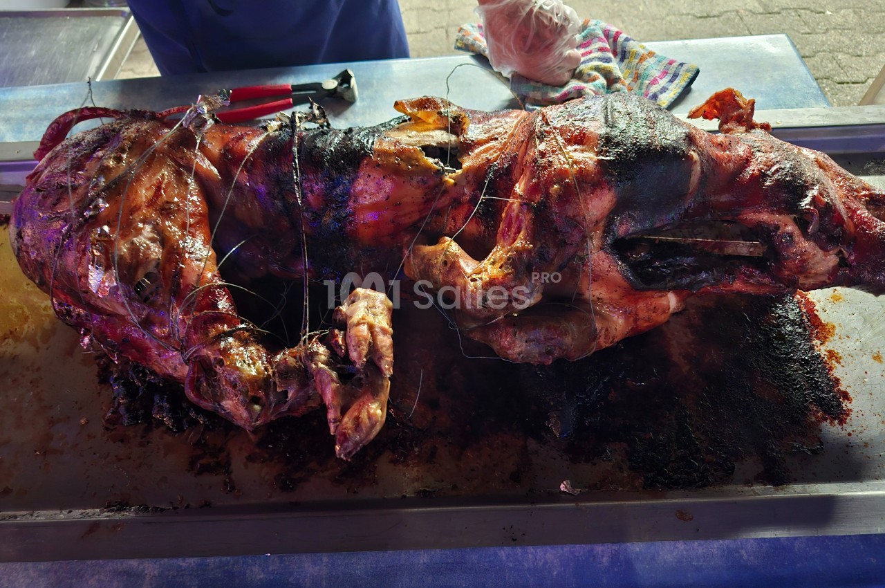 Cochon entier rôti sur une broche, posé sur une table en métal, avec des ustensiles et un torchon à proximité.