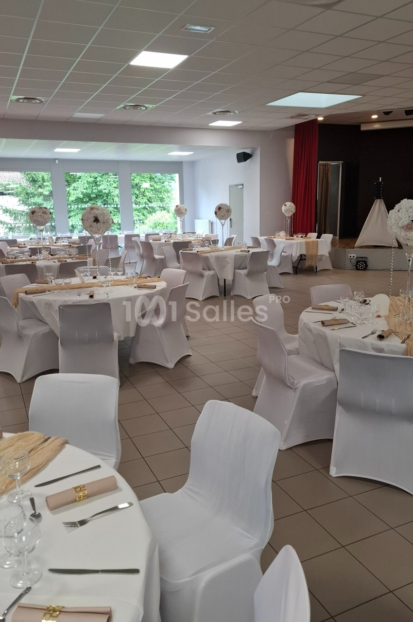 Salle de réception décorée avec des tables rondes, nappes blanches, chaises houssées et centres de table floraux.