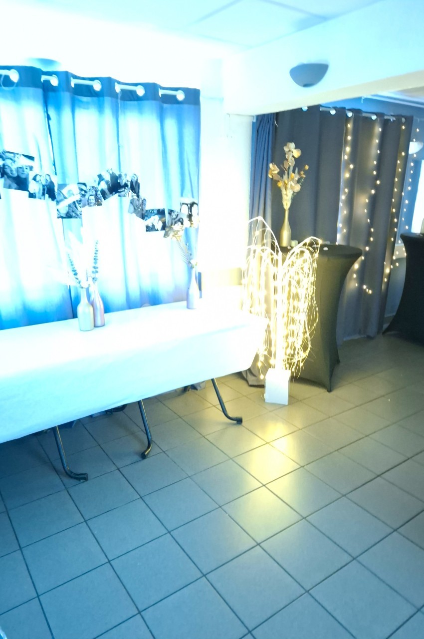 Salle décorée avec rideaux bleus, guirlandes lumineuses, vases avec fleurs et table recouverte d'une nappe blanche.