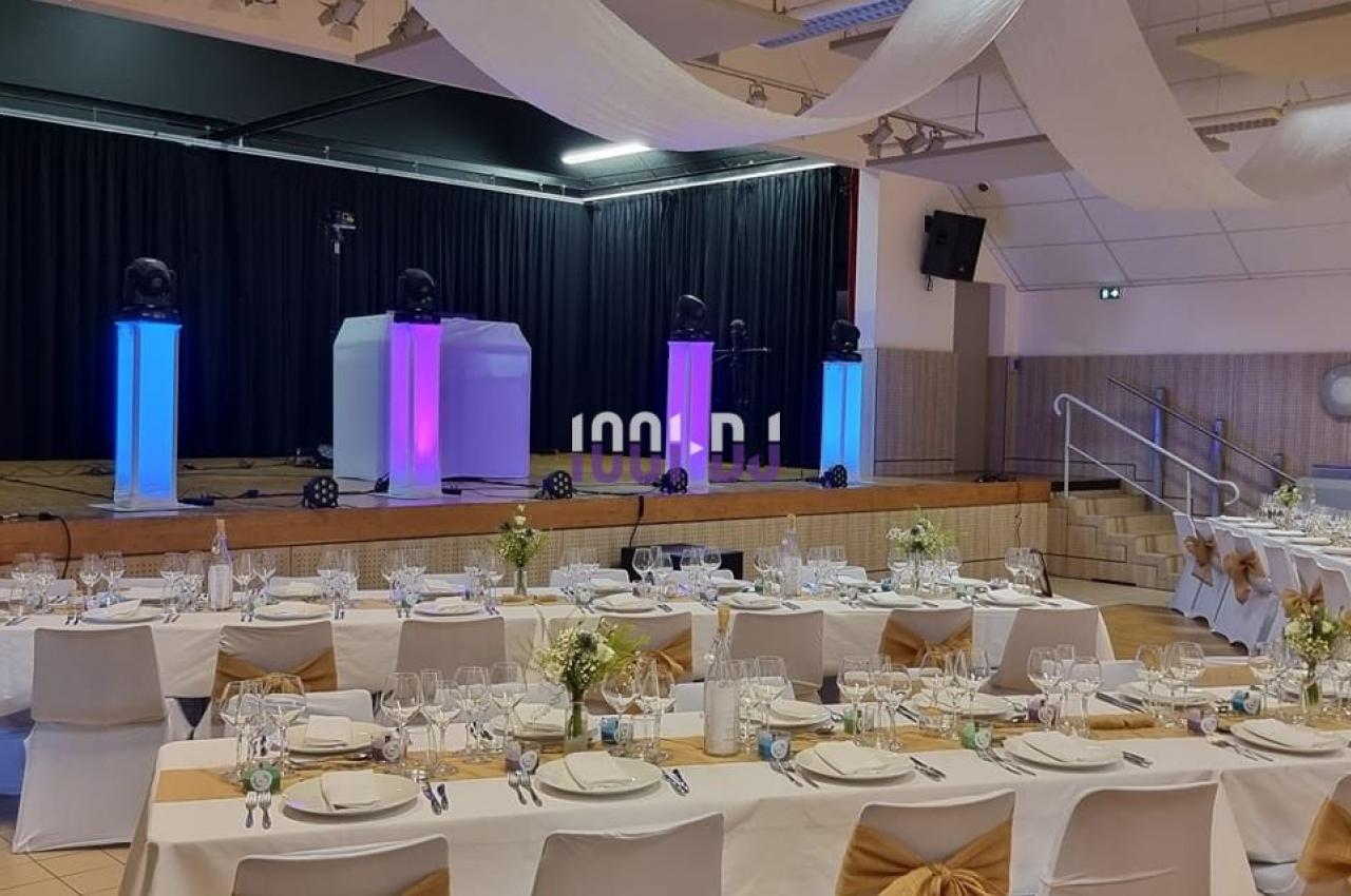 Salle de réception décorée avec des tables dressées et une scène équipée de lumières colorées.