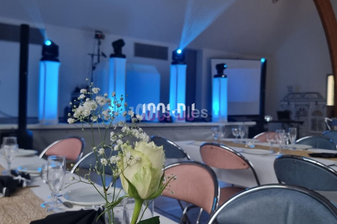 Salle de réception décorée avec des tables dressées et un éclairage bleu mettant en valeur une scène.
