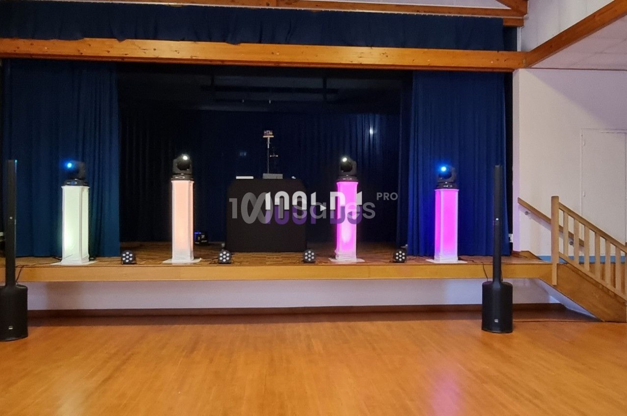 Scène avec éclairage coloré et équipement audio installé dans une salle avec parquet et estrade en bois.