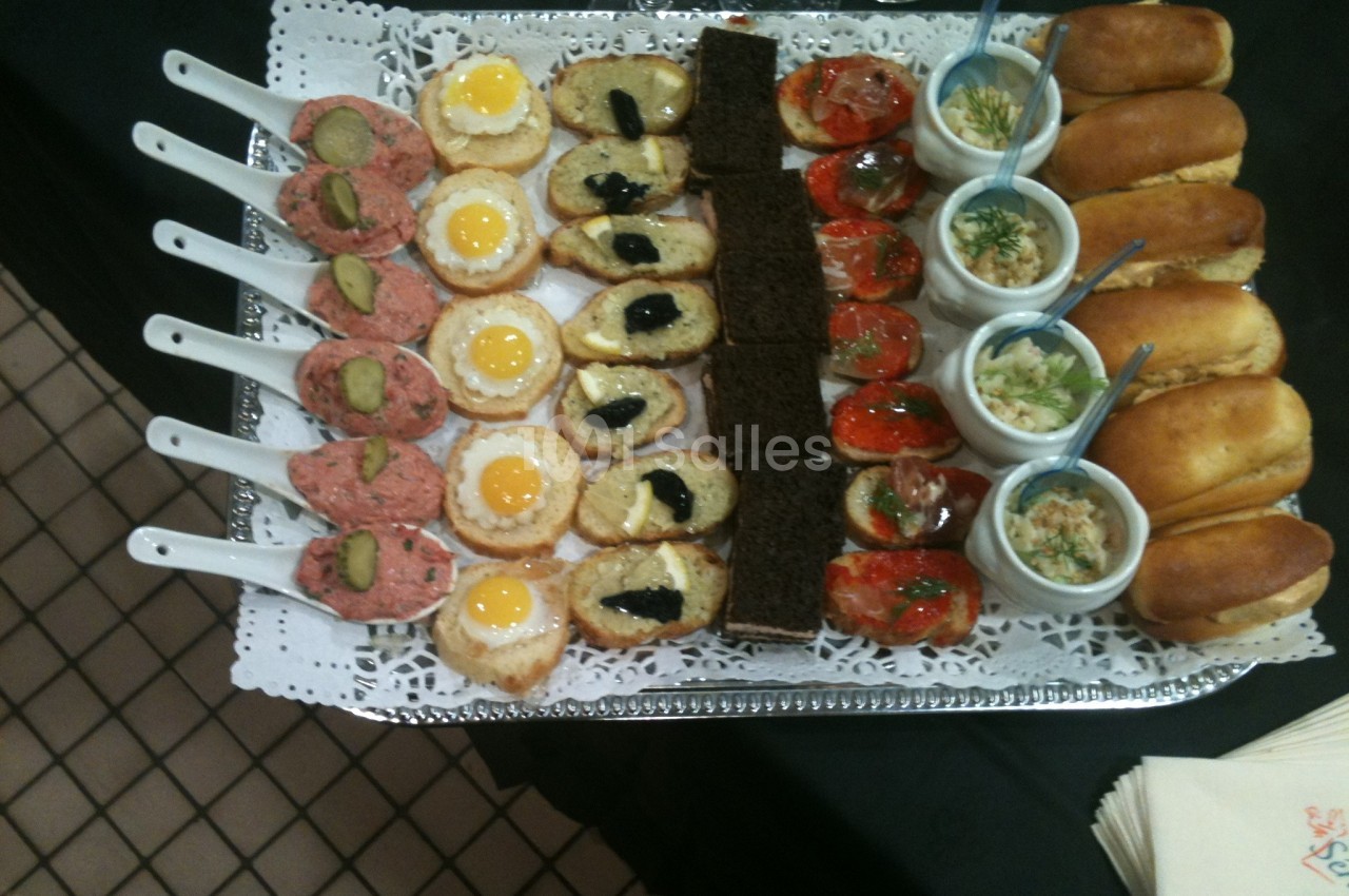 Plateau de canapés variés comprenant œufs de caille, tartinades, pains garnis et verrines sur une nappe noire.