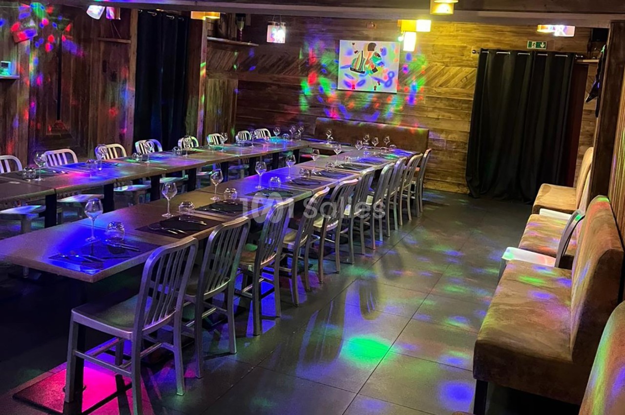Salle de restaurant avec longues tables dressées, éclairage tamisé et effets lumineux colorés sur le sol.