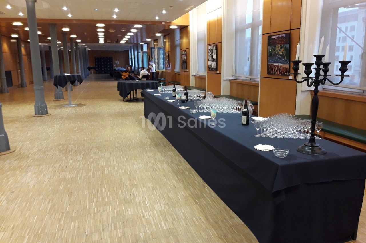 Salle avec tables dressées pour un buffet, comprenant des verres, une bouteille et un chandelier noir.