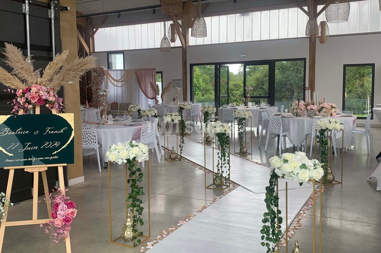 Salle de réception décorée pour un mariage avec allée centrale ornée de fleurs blanches et roses.