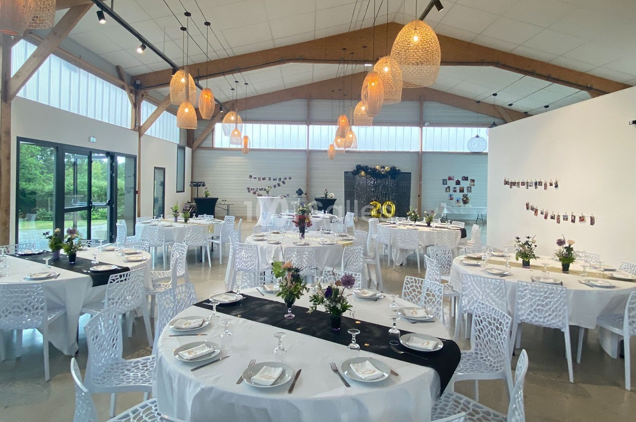 Salle de réception décorée avec des tables rondes dressées, des fleurs et des suspensions lumineuses en rotin.