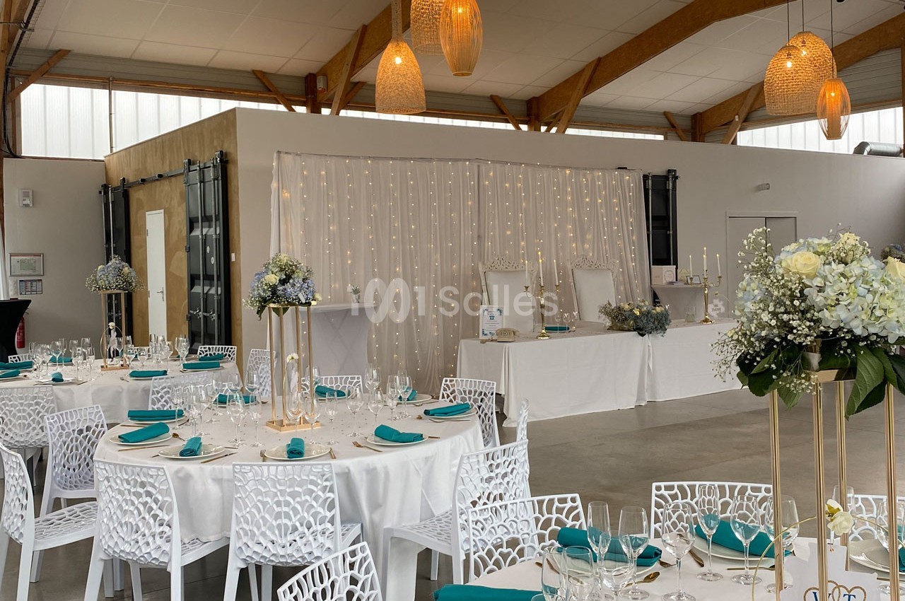 Salle de réception décorée avec des tables rondes, nappes blanches, chaises ajourées et éclairage chaleureux.