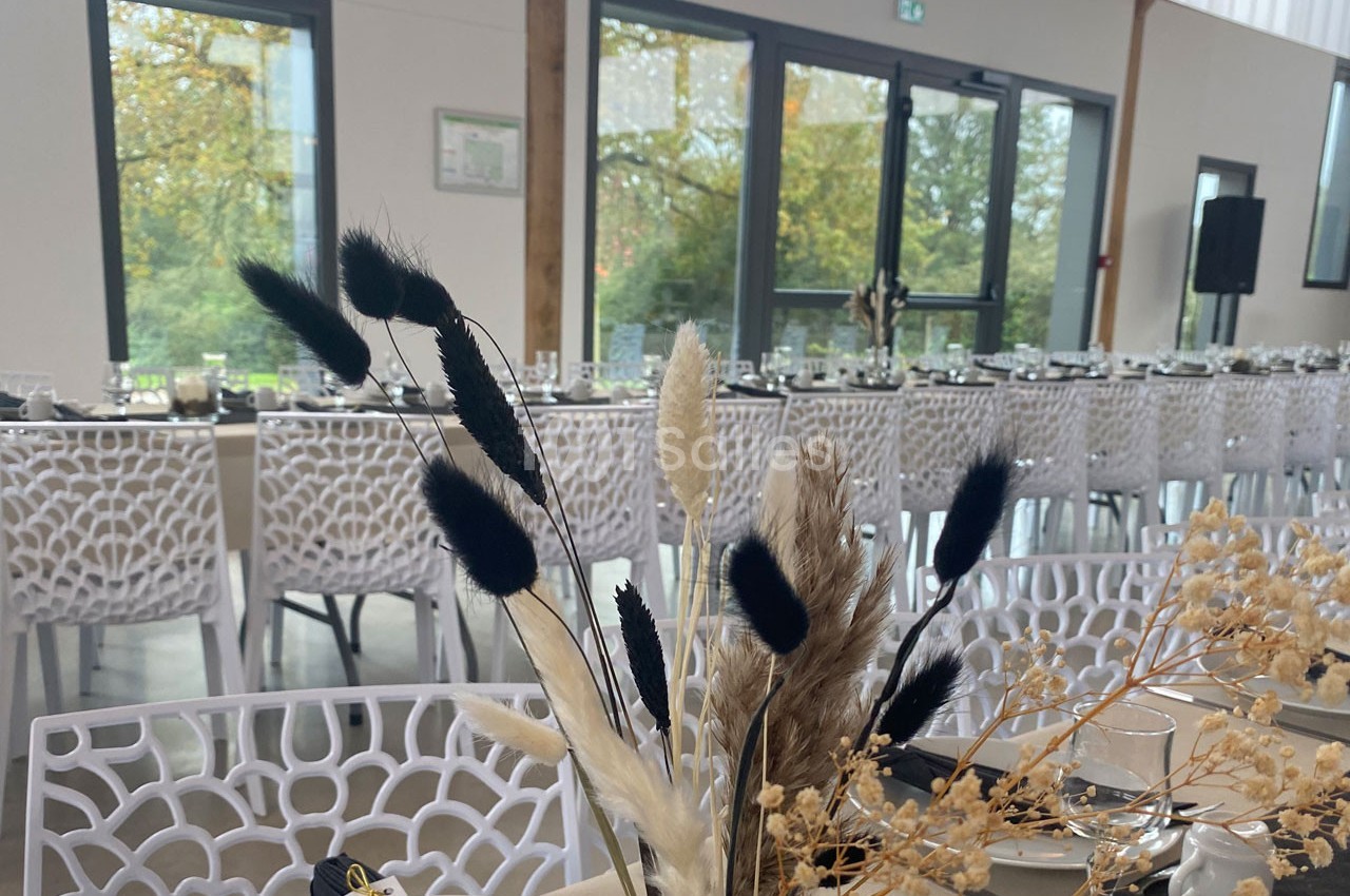Salle de réception lumineuse avec tables dressées et décoration florale en herbes séchées au premier plan.