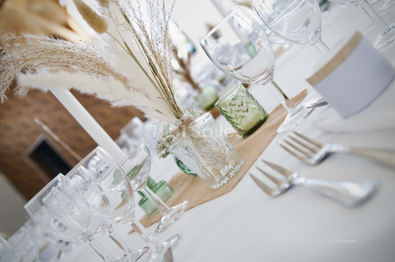 Table décorée avec des pampas, des verres en cristal et des bougies, sur une nappe blanche avec des détails en lin.
