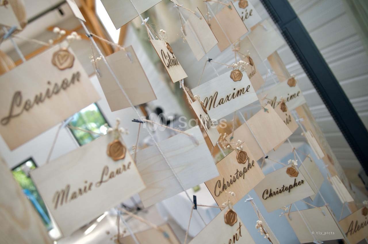 Panneaux en bois suspendus avec des prénoms gravés, alignés dans un espace lumineux.