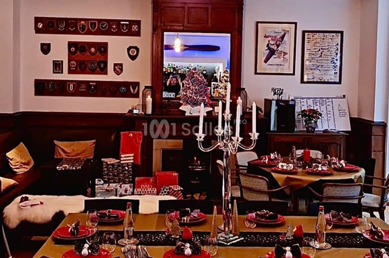 Salle de restaurant décorée avec des tables dressées, un chandelier central et des éléments de décoration murale.