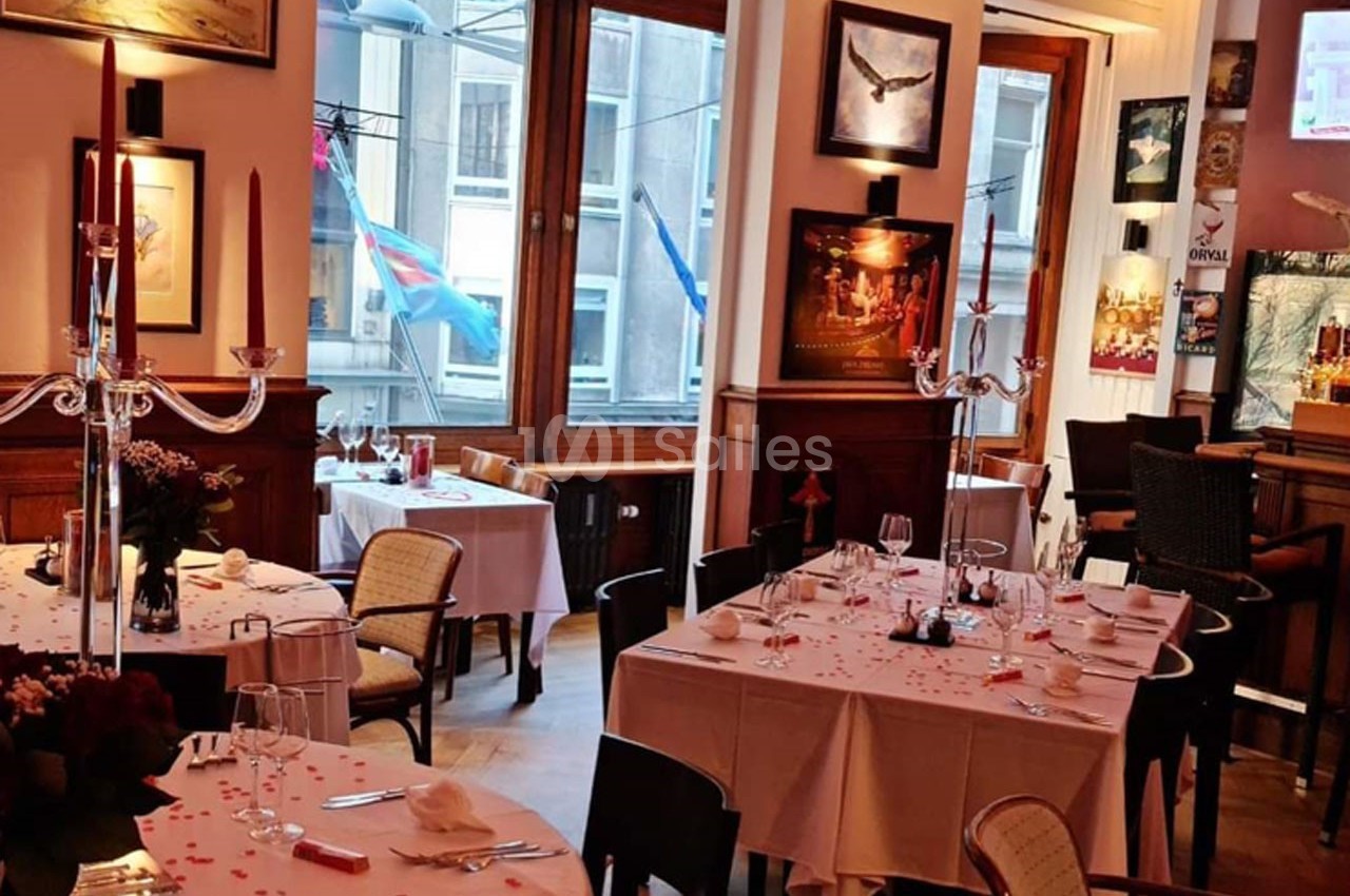 Salle de restaurant élégante avec tables dressées, nappes blanches, chandeliers et vue sur des drapeaux à l'extérieur.