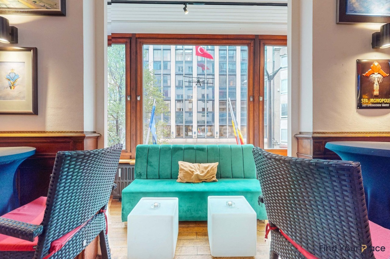 Canapé vert et tables basses blanches dans un salon avec vue sur des drapeaux et des bâtiments à travers une grande fenêtre.