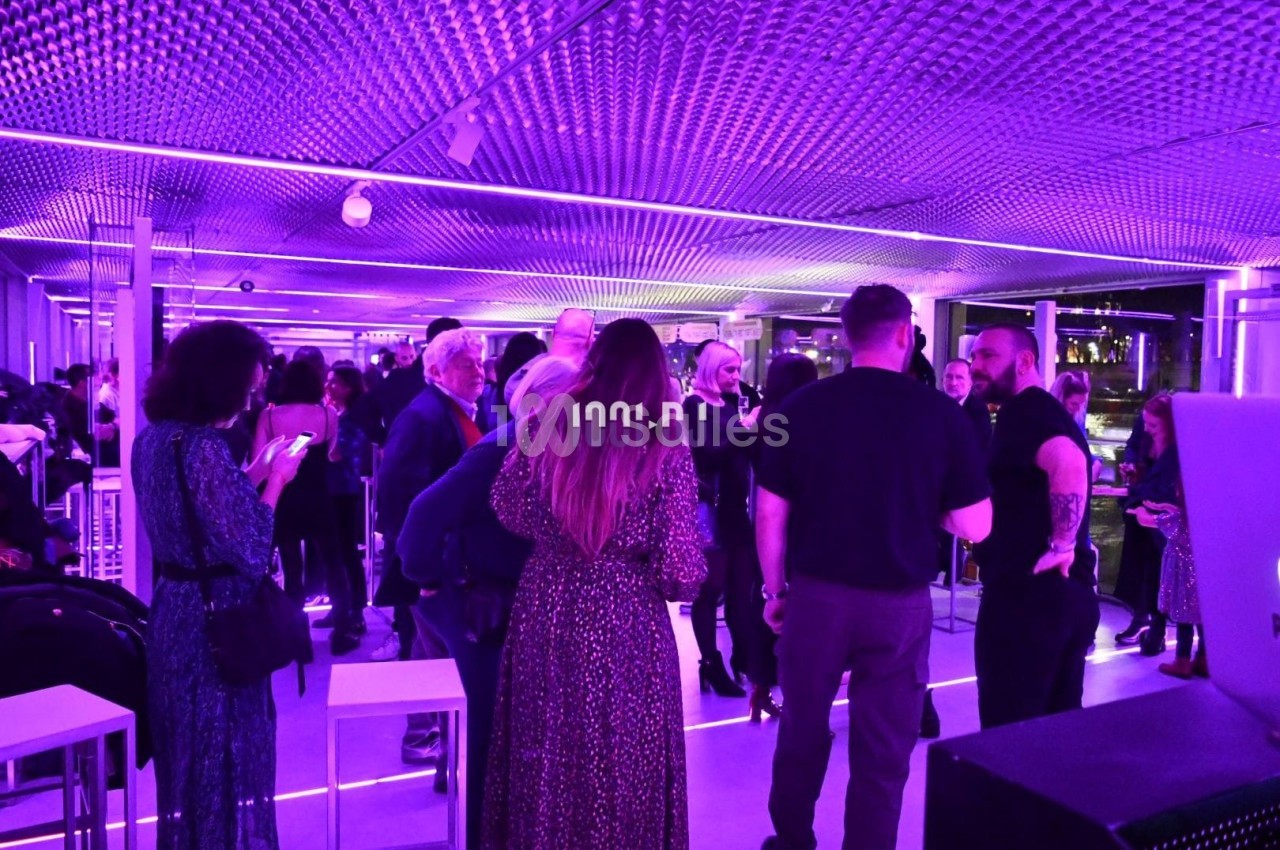 Groupe de personnes échangeant dans un espace intérieur moderne éclairé par des lumières violettes.