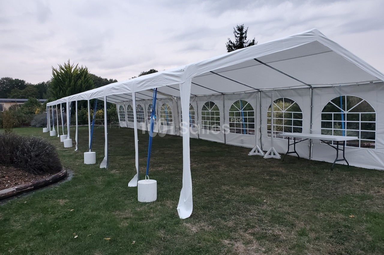 Grande tente blanche montée sur une pelouse, avec des fenêtres en plastique transparent et des tables à l'intérieur.