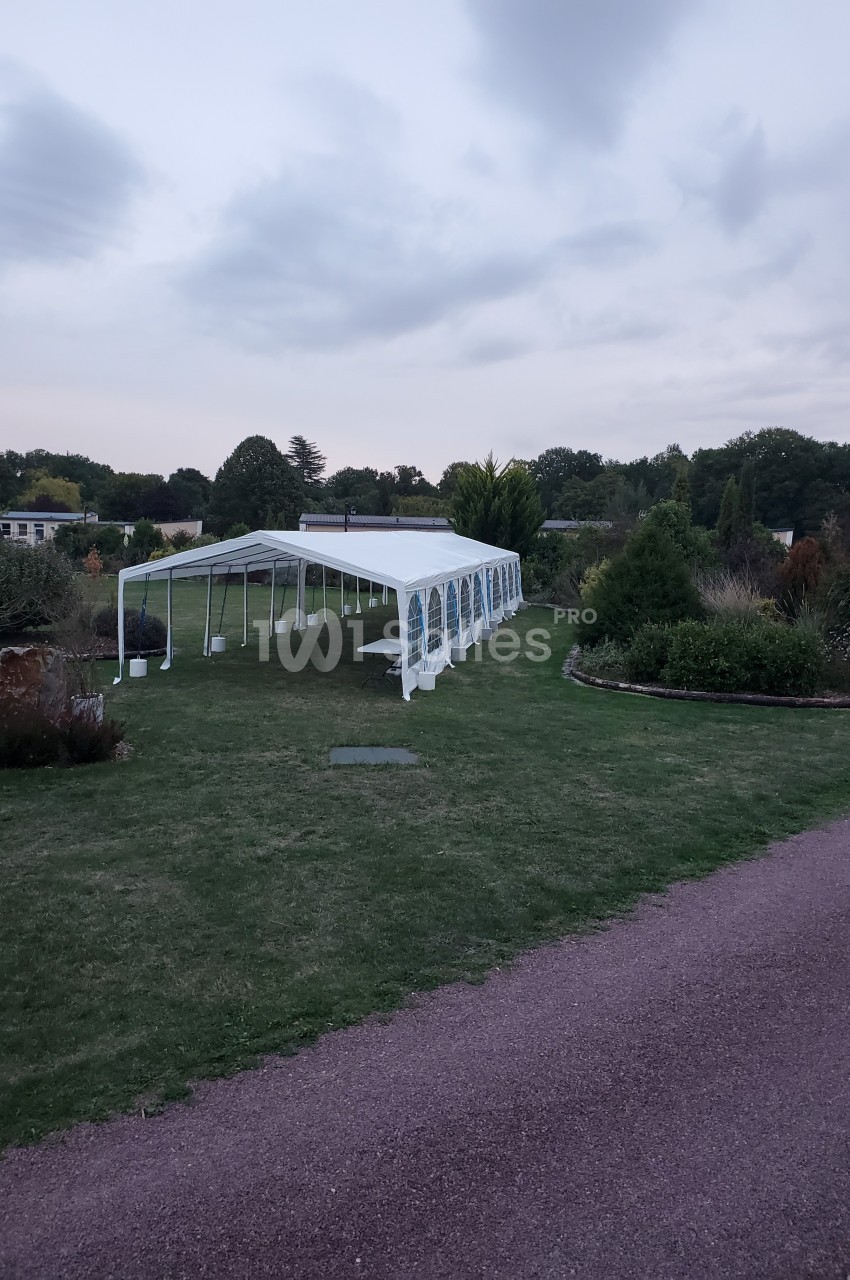 Tente blanche installée sur une pelouse dans un jardin, entourée de végétation et d'un chemin en gravier.