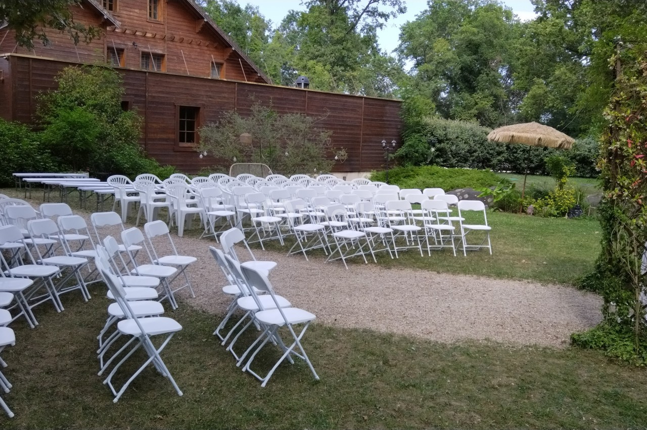 Chaises blanches disposées en rangées sur une pelouse, près d'un bâtiment en bois, pour un événement en extérieur.