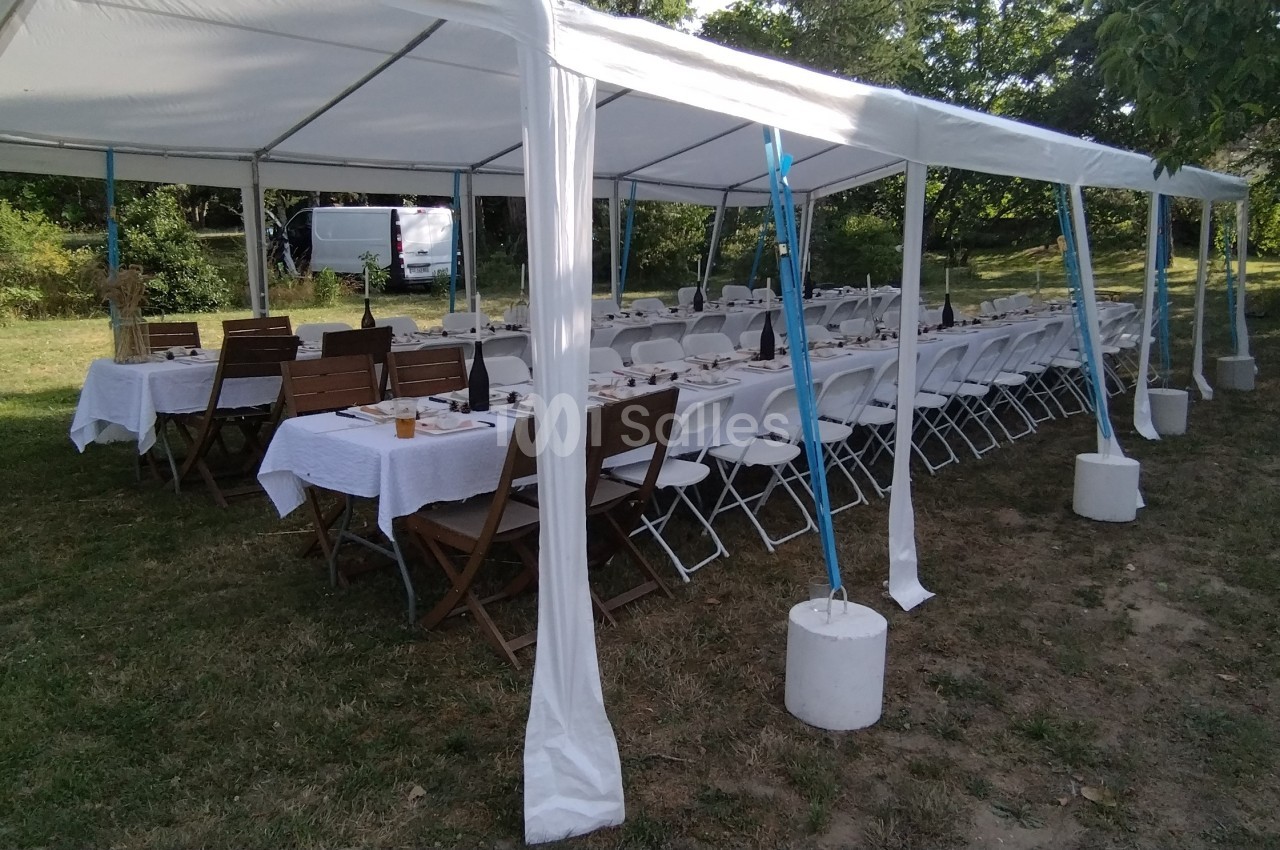 Tables dressées sous une tente blanche dans un jardin, avec des chaises alignées pour un événement en plein air.