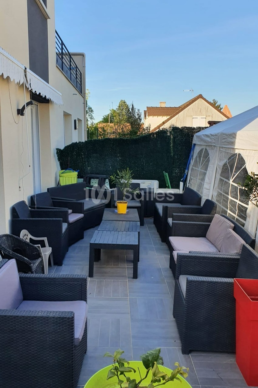 Salon de jardin avec fauteuils en résine tressée, table basse, plantes en pot et tente blanche sur une terrasse carrelée.