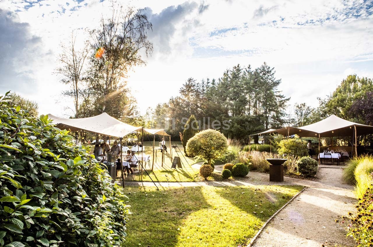 Jardin avec des tentes installées pour un événement, entouré de végétation et baigné par une lumière ensoleillée.