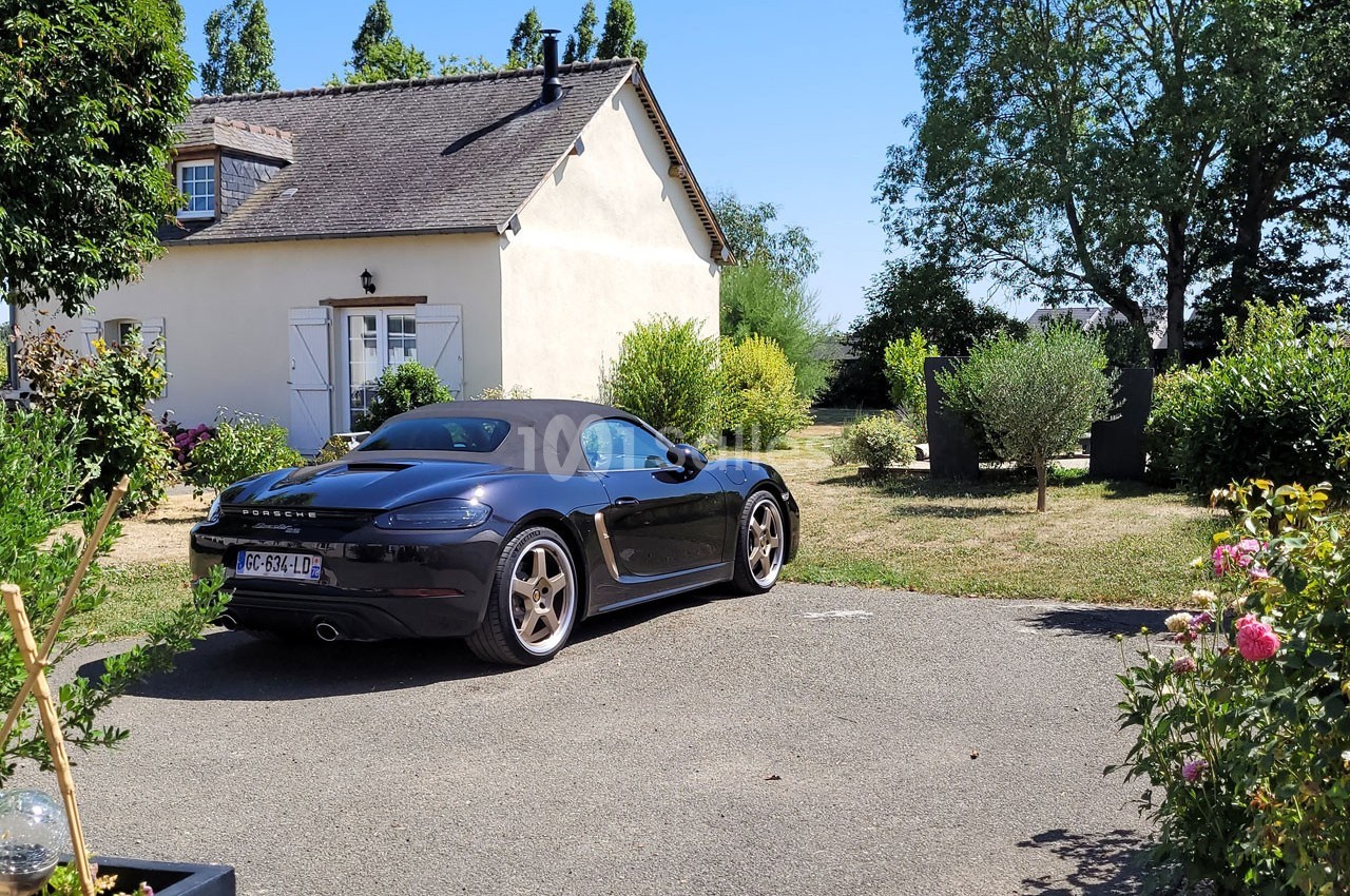 Voiture décapotable noire garée dans une allée devant une maison avec jardin arboré en arrière-plan.