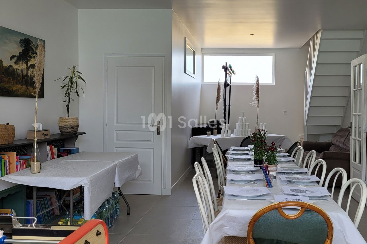 Salle aménagée pour un repas, avec tables dressées, chaises alignées, décorations simples et lumière naturelle.