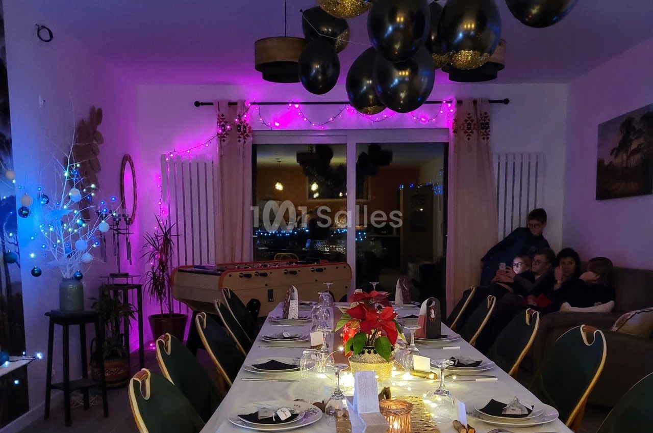 Salle à manger décorée pour une fête avec table dressée, guirlandes lumineuses et ballons noirs suspendus.